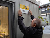 Ein Mann befestigt ein gelbes Schild mit der Aufschrift "i+R" an dem Container.